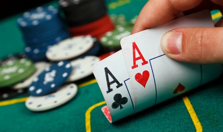 Closeup image of a hand holding an ace of clubs and ace of hearts at a poker table  