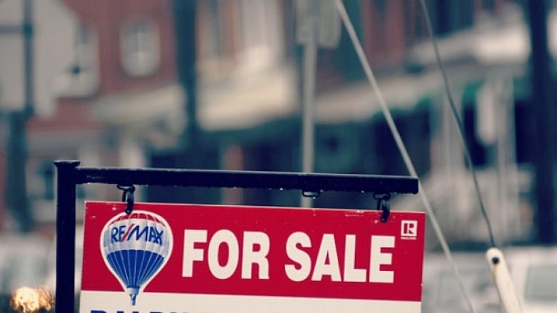 A for sale sign sits in front of a row of blurred out homes.