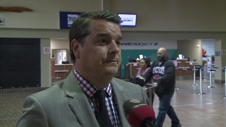 A man in a grey suit standing in an airport terminal. 