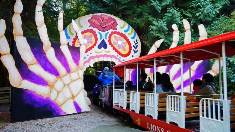 A miniature train enters a skull-like gate in a park.,