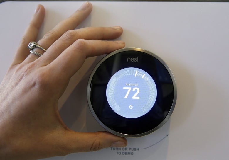 Hand setting a thermostat with a blue screen to 72 F.