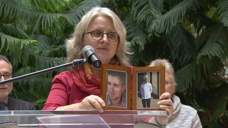 A woman holds a photo of a young man while speaking into a microphone.