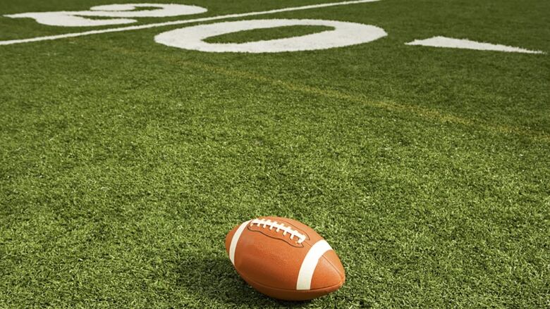 A single football rests on green field turf. 