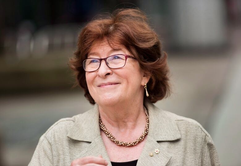 A woman with short, red hair, wearing red-framed glasses, smiles.