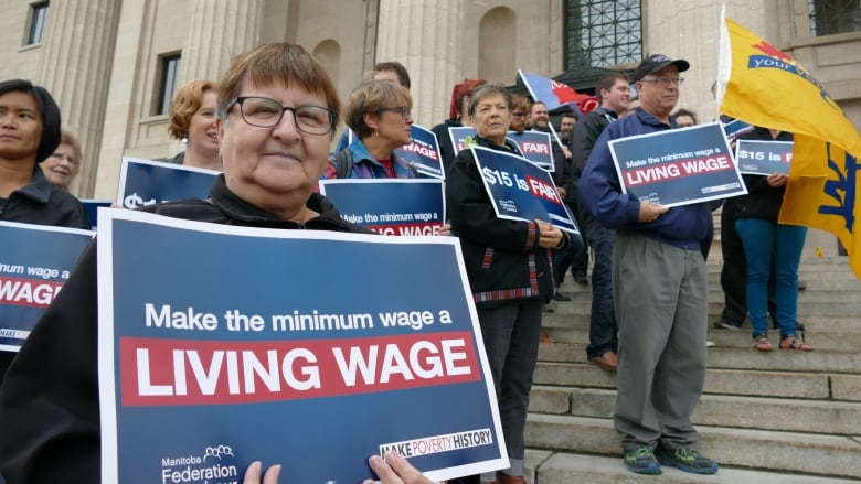 People stand on the wide, concrete steps of a government building, holding signs that say 