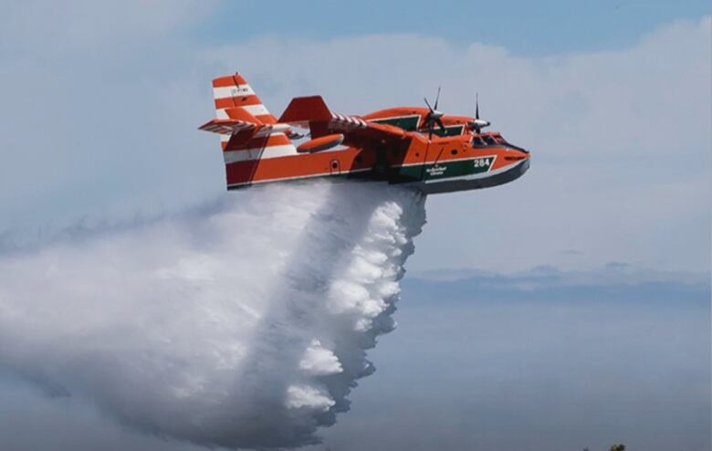 An orange aircraft releases water below it.