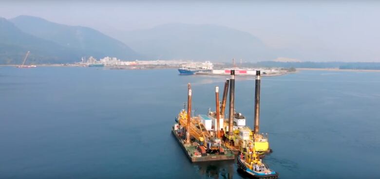 A large ship approaches a port in the distance with moutains behind.