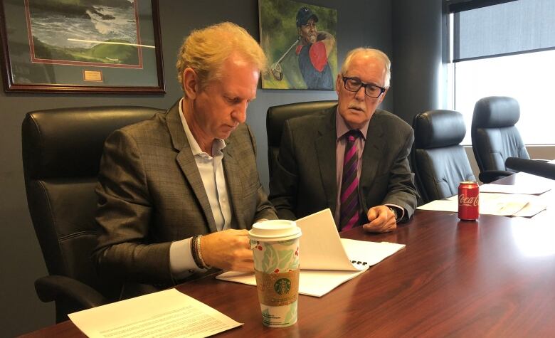 Two men in suits at a boardroom table.