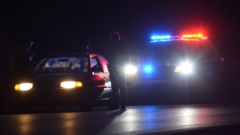 A police vehicle with lights on sits behind a car at night.