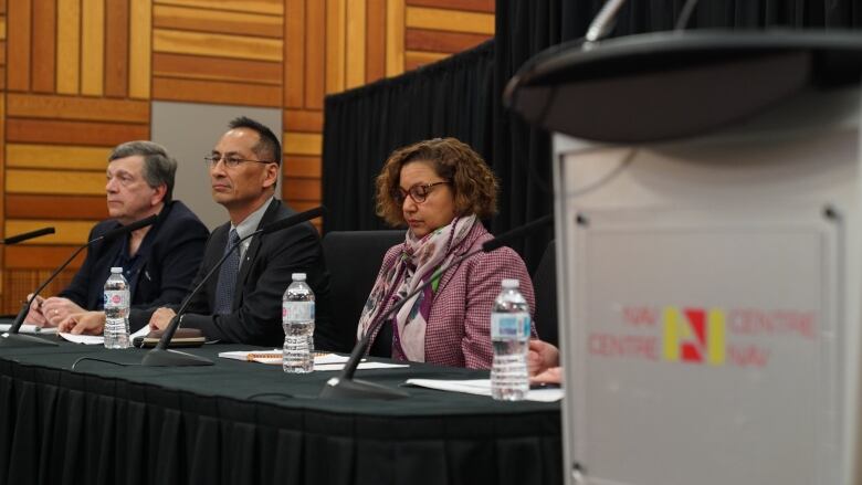 Three government officials sit at a table for a news conference.