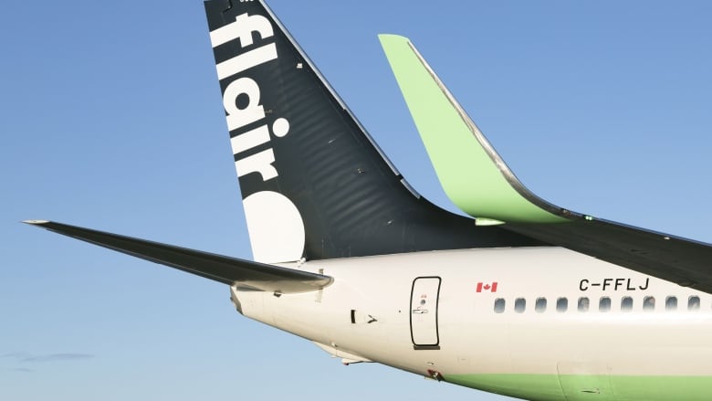 The tail of a plane with the words Flair as it flies in a blue sky.