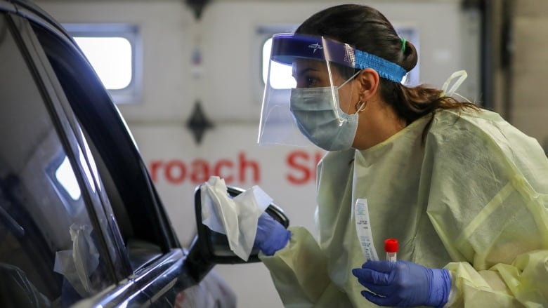 A health-care leans towards a car window, with a testing swab in her hand, as she collects a sample at a drive-thru COVID-19 testing facility in Alberta. 