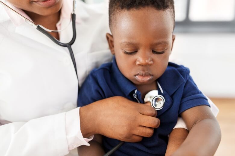 A closeup shows a doctor holding a stethoscope to the chest of a toddler.