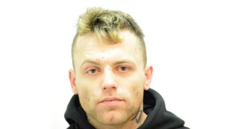 A tattooed man in a black hoodie poses for a mug shot.