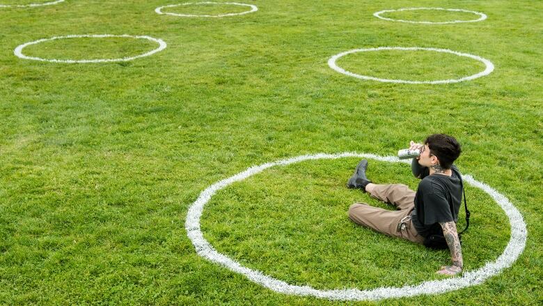 A man sips beer outdoors in a field of grass.