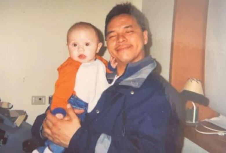 A man with a jacket, smiling and hold a baby. 