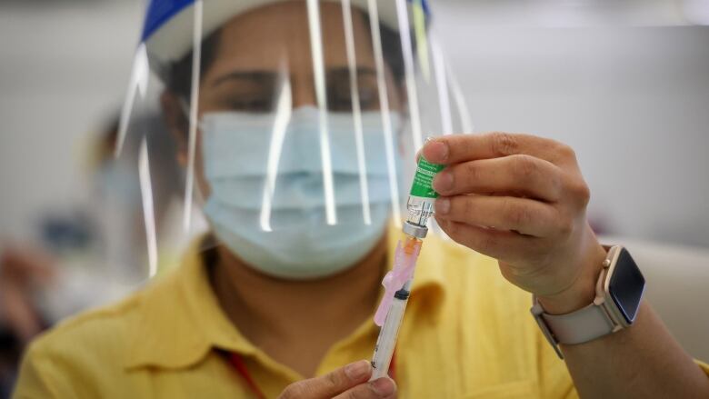 A health care worker in a mask and face shield prepares a syringe with the COVID-19 vaccine.