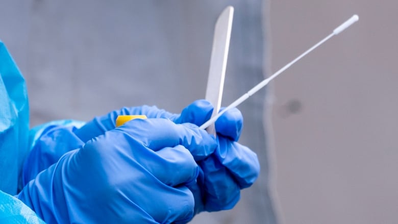 A nurse wearing blue gloves handles a COVID-19 test swab. 