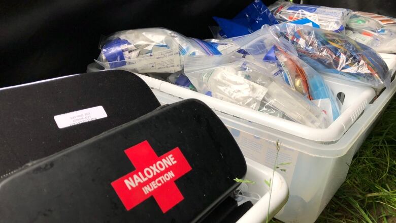 A black Naloxone kit with a red cross sits in a bin next to another bin with medical supplies.