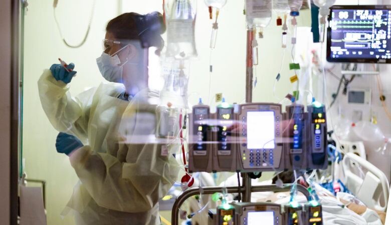 A nurse can be seen, behind IV bags and monitors,  working in an intensive care unit