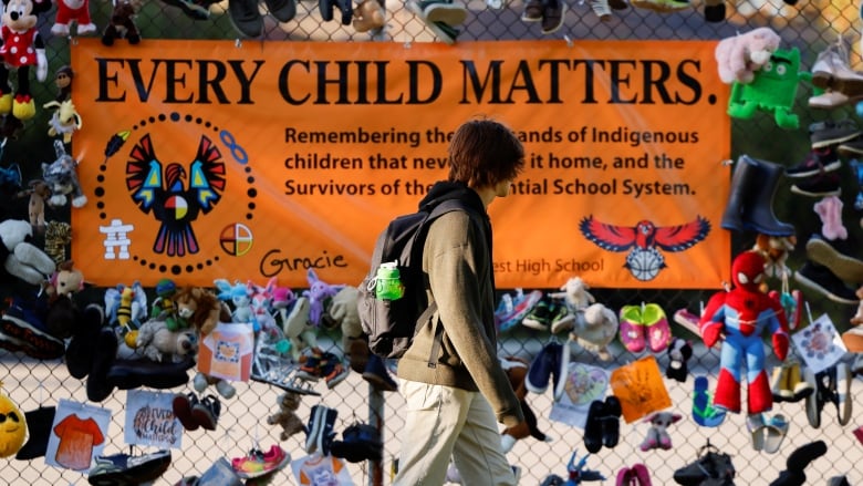 a person walks by an every child matters sign on a fence.