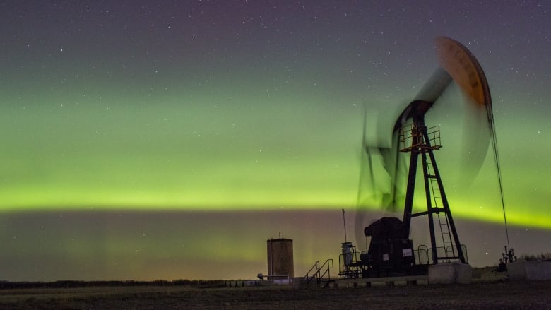 An oil pumpjack operates at night beneath the northern lights.