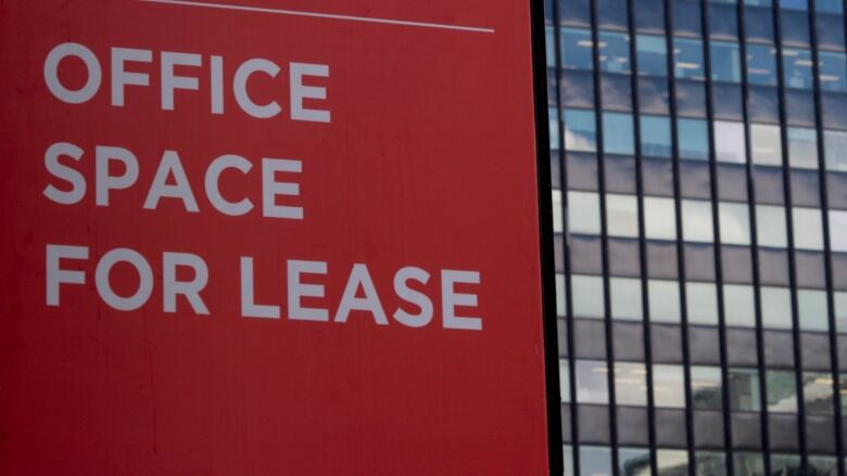 Red sign in front of glass office building. The sign reads 