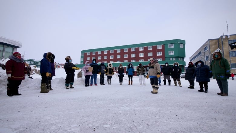 A woman wearing heavy winter clothing surrounded by others wearing similar clothes standing outside in the snow