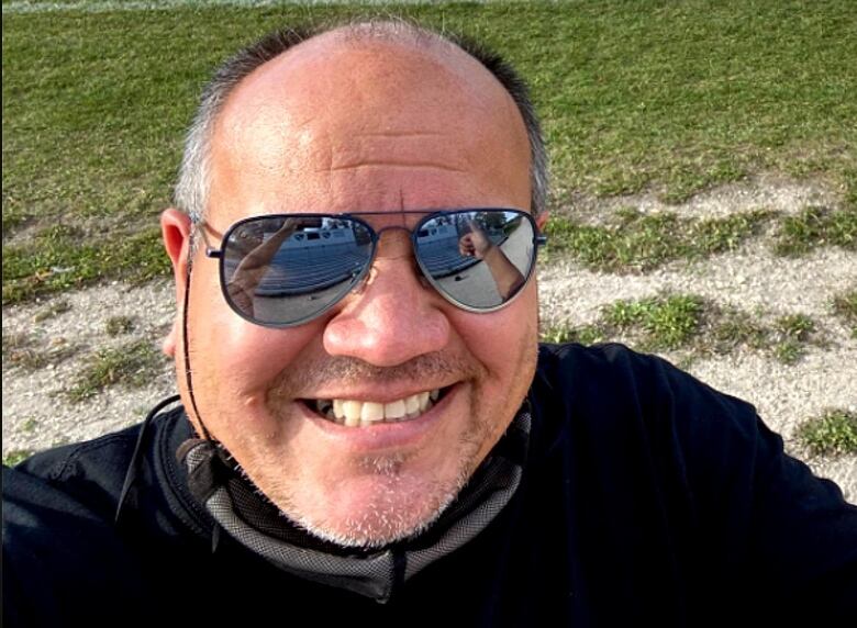 A man in aviator sunglasses smiles for the camera with a lawn in the background.