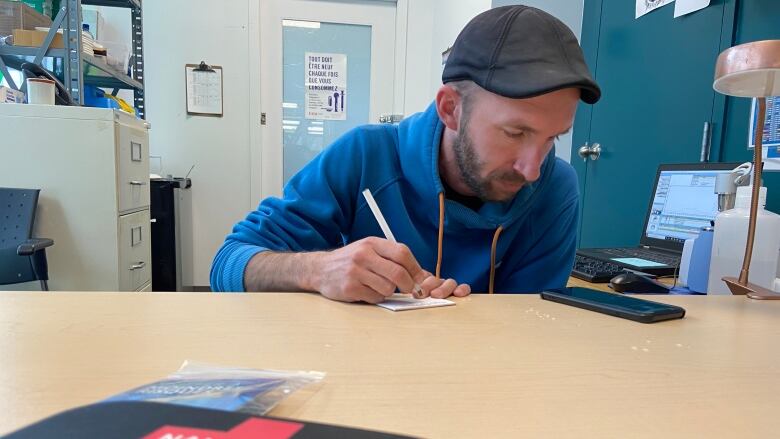 Jean-Franois Mary, executive director of CACTUS Montral, a harm reduction organization, sits at a table and writes. In the foreground, a naloxone kit can be seen on the table.