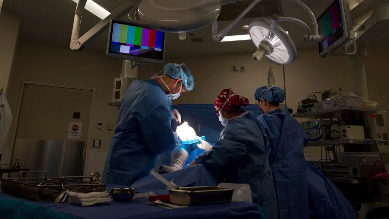 A number of surgeons in an operating theatre, with blue gowns and PPE on.