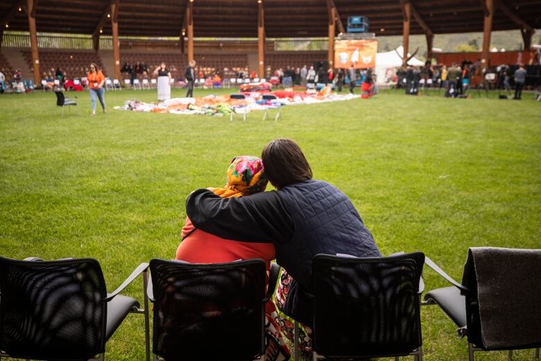 Two people sit in lawn chairs, one with their arm around the other