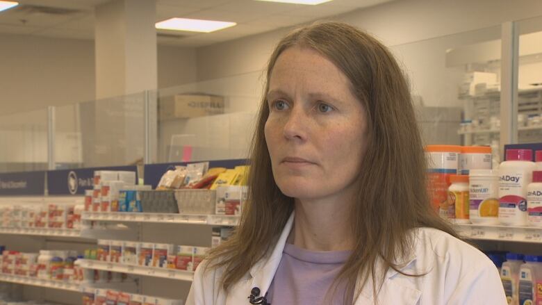 Pharmacist Diane Harpell stands in front of a shelves of vitamins and cold medicine inside a pharmacy.