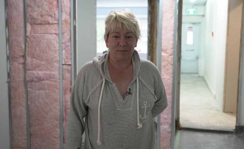 A woman standing in front of unfinished renovations beside her own apartment unit.