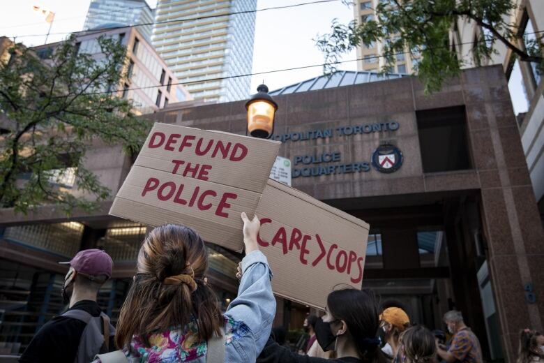 Protestors hold up signs saying defund the police outside Toronto police headquarters