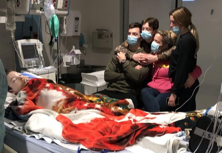 A couple and their two grown children embrace at the bedside of a dying child in intensive care.