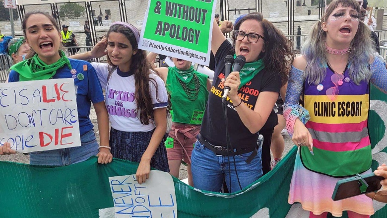 Women protest on a street, waving pro-choice signs.