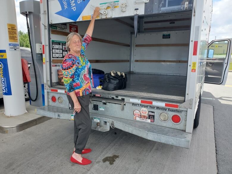 A woman closes the back of a U-Haul moving van. The van is parked next to a gas pump.