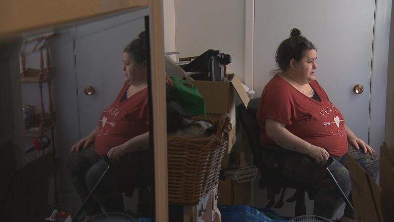 A woman sits in her apartment, boxes of her belongings beside her. 