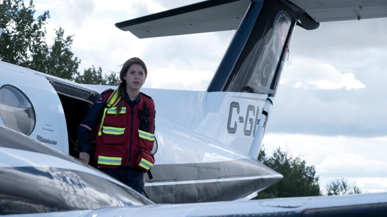 A woman in a reflective vest leans outside of a small airplane with a distressed look on her face. 