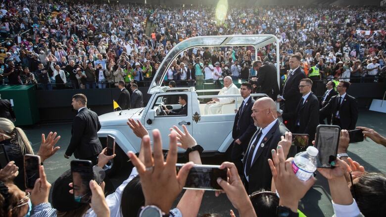 A white open-air vehicle carries Pope Francis through crowds of people.