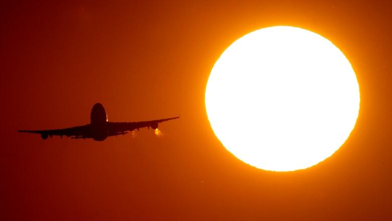 An airplane in flight is framed next to the sun.