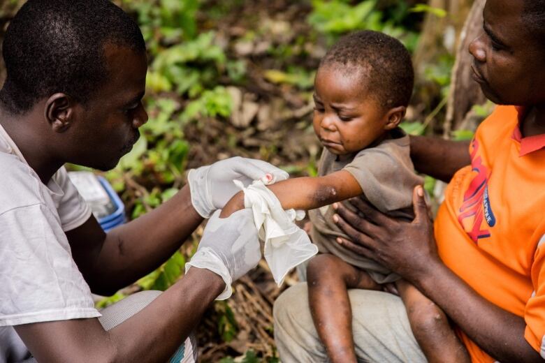 A man wearing surgical gloves, a toddler on his father's knee. All three are African.