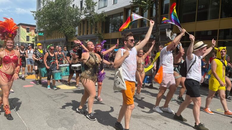 People waving rainbow flags walk down Sainte-Catherine Street. 