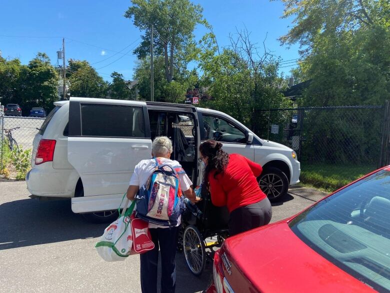 A woman helps guide her husband into a para-transit van alongside its driver.