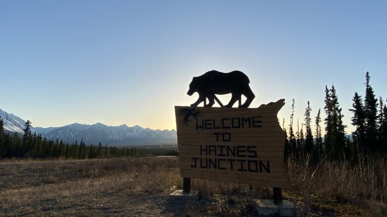 A silhouette of the Welcome to Haines Junction sign at sunrise with snowy mountains in the background.  