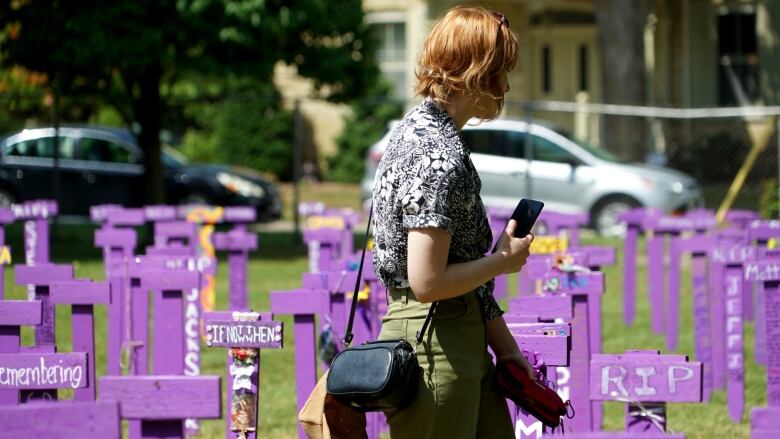 A young woman walks by purple wooden markers in a field. 