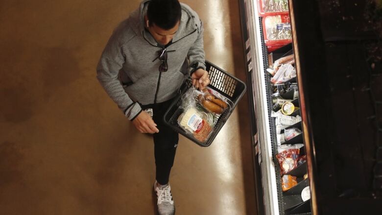 A man shops for groceries with a hand-held basket