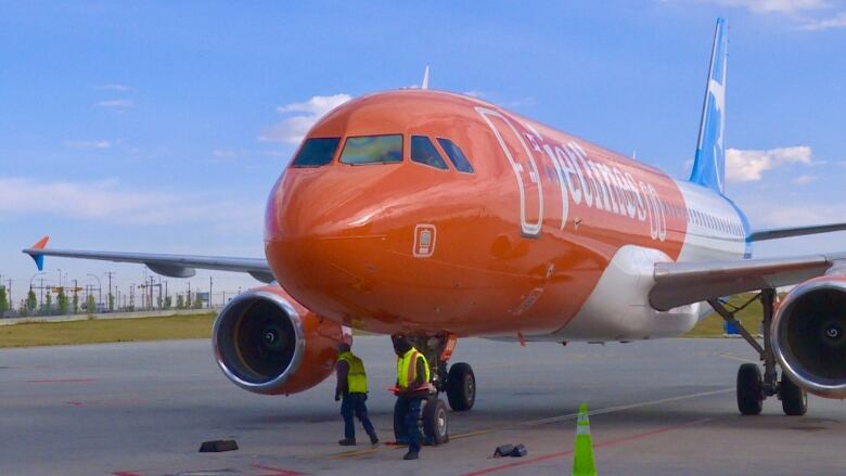 Orange, blue and white Canada Jetlines plane on tarmac, taken from a front angle