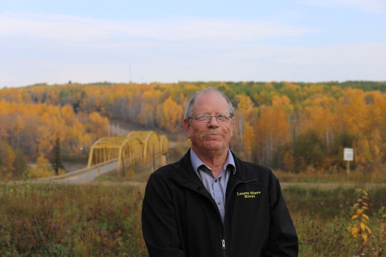 Reeve stands in front of the Athabasca River and a yellow bridge.